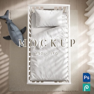 Peut inclure: Un lit bébé blanc avec de la literie blanche, dont un oreiller et une couette, est posé sur un tapis de couleur claire. Un jouet en peluche en forme de requin gris repose sur le tapis. Le texte "MOCKUP" et "PSD + JPG" est inclus.