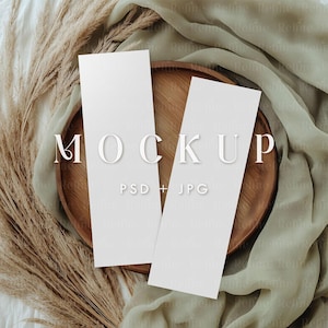 Puede incluir: Dos tarjetas blancas en blanco sobre una bandeja de madera con un tejido beige y hierba seca en el fondo. El texto "MOCKUP PSD + JPG" está impreso en las tarjetas.