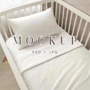 May include: A white crib with a white pillow and sheet set. The word "MOCKUP" is displayed across the pillow and sheet. The text "PSD + JPG" is below the word "MOCKUP".