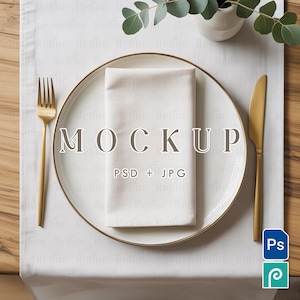 May include: A white plate with a gold rim, a folded white napkin, and gold cutlery are arranged on a white tablecloth. The word "MOCKUP" is printed on the plate, along with "PSD + JPG".