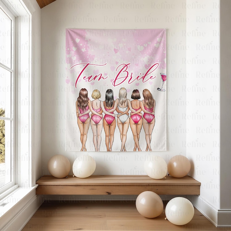 K&ouml;nnte beinhalten: Ein rosa Wandteppich mit den Worten "Team Bride" und einer Illustration von sechs Frauen in Badeanz&uuml;gen. Der Wandteppich h&auml;ngt an einer Wand &uuml;ber einer Holzbank mit mehreren beigen Luftballons.
