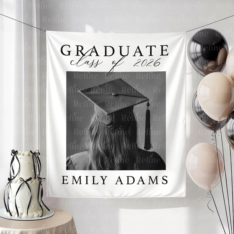 May include: A white graduation banner with the text "GRADUATE class of 2026" and "EMILY ADAMS". The banner features a black and white photo of a person wearing a graduation cap. Balloons and a cake are also visible.