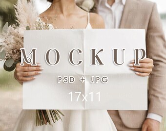 Puede incluir: Una maqueta de papel blanco con la palabra "MOCKUP" en letras marrones, sostenida por una pareja. También se ve el texto "PSD + JPG" y "17x11". La pareja está vestida con atuendos de boda, con la novia sosteniendo un ramo.