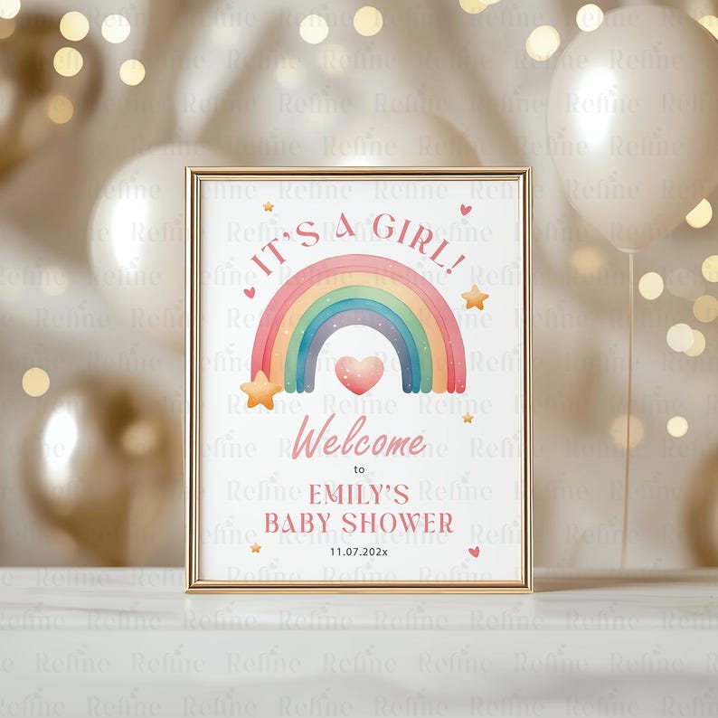 May include: A white sign with a gold frame announcing a baby shower. The sign features a rainbow with a pink heart in the center and the text "It's a girl! Welcome to Emily's Baby Shower 11.07.202x".