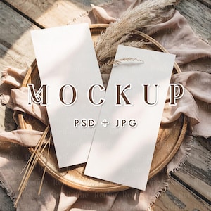 May include: Two blank white cards on a wooden tray with dried pampas grass and a beige fabric background. The text "MOCKUP PSD + JPG" is printed on the cards.