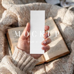 Può includere: Un mockup di una carta bianca vuota tenuta da una mano che indossa un maglione color crema. La carta è in posizione verticale e ha il testo "MOCKUP PSD + JPG" stampato su di essa. La carta è a fuoco e la mano e il maglione sono sfocati sullo sfondo.