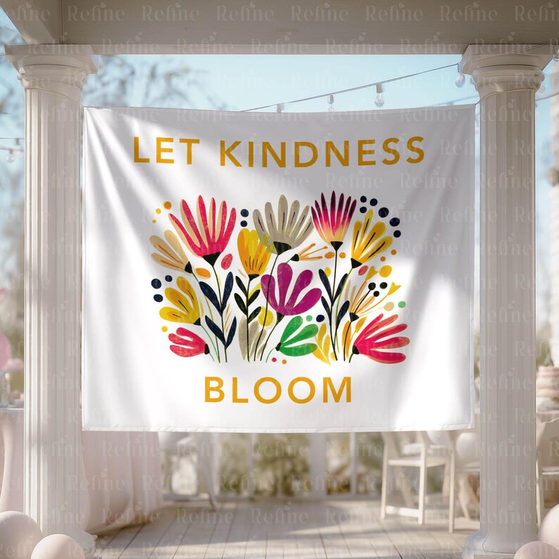 May include: White banner with the words "LET KINDNESS BLOOM" in gold lettering. The banner features a colorful floral design with red, yellow, purple, and green flowers. The banner is hanging outdoors.