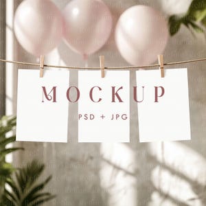 May include: Three white cards with the text "MOCKUP PSD + JPG" hanging on a string with clothespins. The cards are in front of a blurred background of pink balloons.