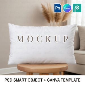 Puede incluir: Una almohada rectangular blanca con la palabra "MOCKUP" impresa, colocada sobre un pequeño taburete de madera. El fondo incluye plantas secas y un sofá. La imagen también presenta los logotipos de Photoshop, Canva y otra plataforma de diseño.