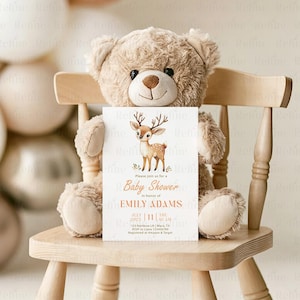 Peut inclure: Une invitation de baby shower avec une illustration de cerf, tenue par un ours en peluche sur une chaise en bois. L'invitation indique "Baby Shower" et comprend le nom "Emily Adams", la date, l'heure et les d&eacute;tails RSVP. L'ours en peluche est brun clair.