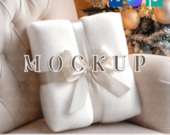 May include: A folded white blanket tied with a satin ribbon, presented on a cream-colored tufted armchair. The word "MOCKUP" is overlaid on the blanket. The text "PSD SMART OBJECT + CANVA TEMPLATE" is at the bottom.