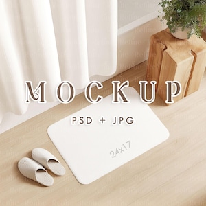 以下が含まれることがあります： 「MOCKUP」と「PSD + JPG」の文字がプリントされた、61x43 cmの白い長方形のバスマット。2足のライトベージュのスリッパがマットの横にあります。シーンは木の床に設定されています。