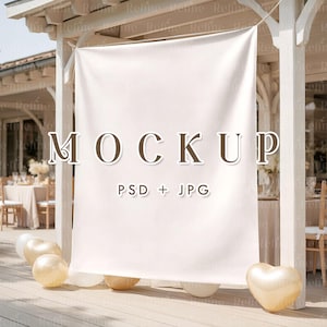 May include: A white banner with the word "MOCKUP" in brown letters, and the text "PSD + JPG" below it. The banner is hanging on a wooden structure, with gold and white balloons at the bottom. The scene is outdoors.