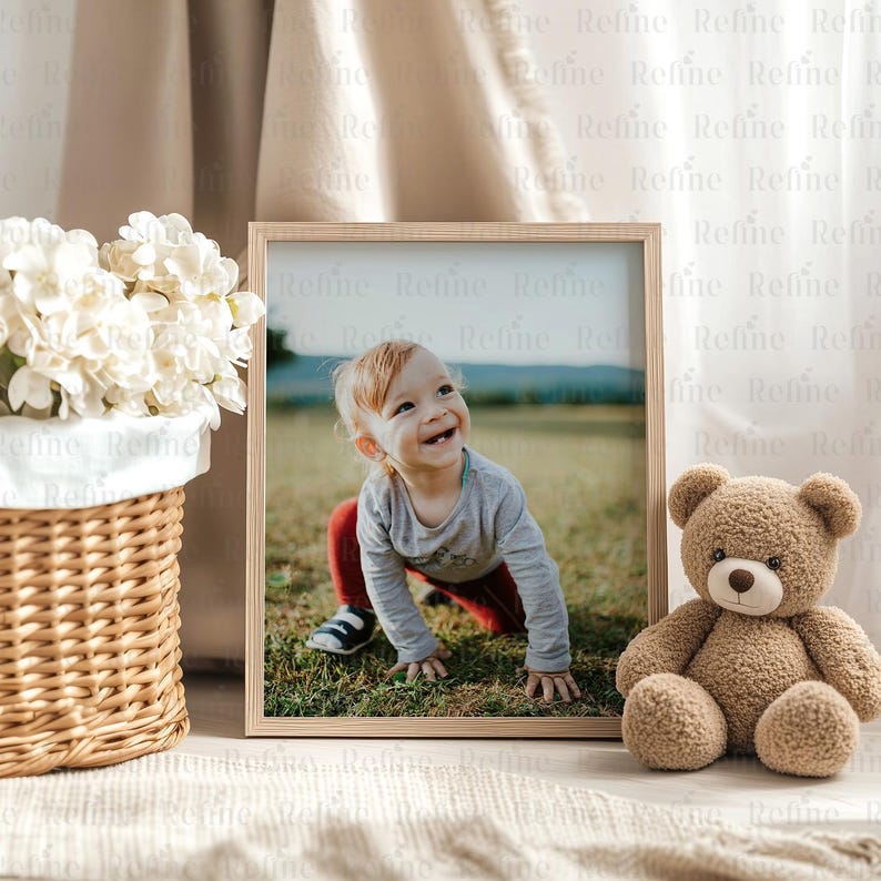 May include: A framed photograph of a young child smiling and crawling on a grassy field. The photo is displayed on a table next to a brown teddy bear.