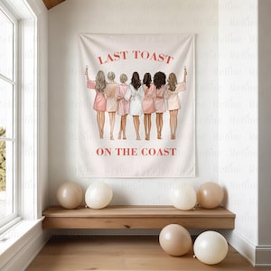 K&ouml;nnte beinhalten: Ein wei&szlig;es Wandtuch mit dem Text "LAST TOAST ON THE COAST" in Rot. Das Wandtuch zeigt sieben Frauen in Badem&auml;nteln, die mit Gl&auml;sern ansto&szlig;en. Beige Luftballons liegen auf einer Holzbank.