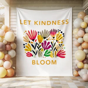 K&ouml;nnte beinhalten: Wei&szlig;es Banner mit den Worten "LET KINDNESS BLOOM" in Gold. Das Banner zeigt ein farbenfrohes Blumendesign mit roten, gelben und lila Blumen. Das Banner h&auml;ngt drau&szlig;en.