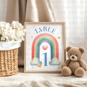 May include: A rainbow table number sign with a blue heart and the number 1 in the center. The sign is framed in wood and has a white background with gold stars and raindrops.