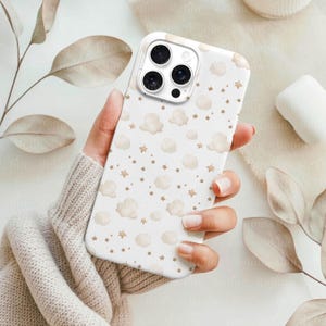May include: White phone case with a pattern of beige clouds and stars. The case has a glossy finish and a camera cutout. The design is repeated across the entire surface of the case. The phone case is held in a person's hand.