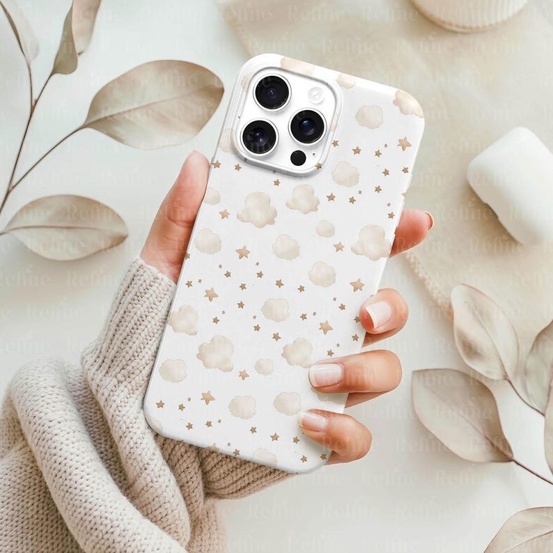 May include: White phone case with a pattern of beige clouds and stars. The case has a glossy finish and a camera cutout. The design is repeated across the entire surface of the case. The phone case is held in a person's hand.