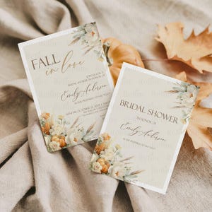 May include: Two beige bridal shower invitations with floral and pumpkin accents. One invitation reads "Fall in Love" and the other says "Bridal Shower". Both include the name "Emily Anderson".