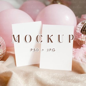 Op de afbeelding: Twee witte rechthoekige kaarten met het woord "MOCKUP" in bruine letters. De tekst "PSD + JPG" staat onder het woord. De kaarten liggen op een glinsterend, lichtgekleurd oppervlak, met roze ballonnen en discoballen op de achtergrond.