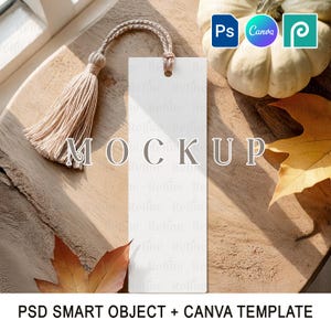 Könnte beinhalten: Ein weißes Lesezeichen mit beigem Quasten, mit dem Wort "MOCKUP" in Grau. Das Lesezeichen liegt auf einer Holzoberfläche, mit einem kleinen weißen Kürbis und Herbstblättern. Der Text "PSD SMART OBJECT + CANVA TEMPLATE" befindet sich unten.
