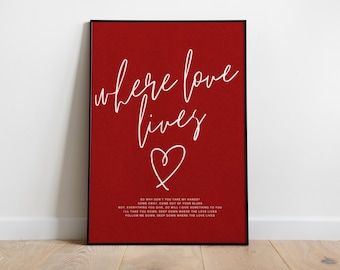May include: Framed art print with a red background and white cursive text that reads "where love lives" with a heart symbol. Below the main text is a smaller text block with song lyrics.