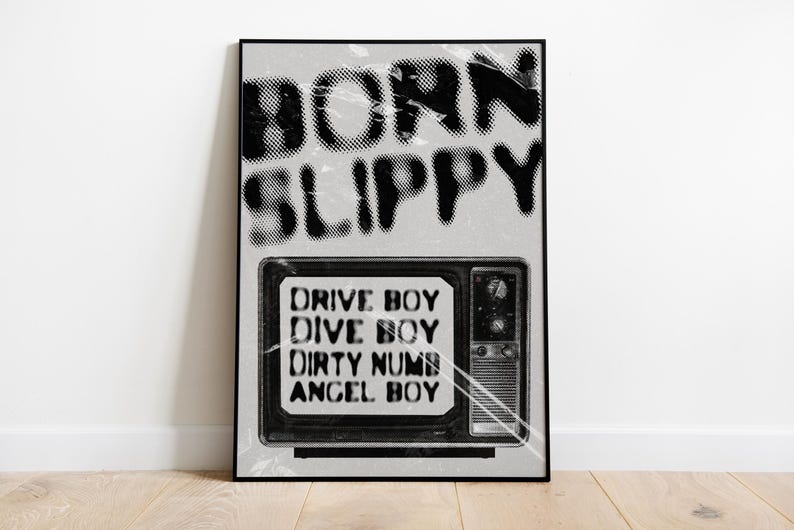 May include: Black and white poster with the text "Born Slippy" in a bold, graffiti-style font. Below the text is a black and white image of a vintage television with the text "Drive Boy, Dive Boy, Dirty Numb, Angel Boy" displayed on the screen.