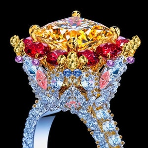 Op de afbeelding: Een gouden ring met een grote, gele middelste steen omringd door kleinere rode, roze, blauwe en gele stenen. De ring is gezet in een bloemmotief.