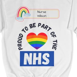 May include: White hoodie with a rainbow heart and the text "Proud to be part of the NHS" in a blue rectangle. A rainbow with clouds and a name tag that says "Nurse Wilson" is above the heart.