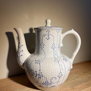 Op de afbeelding: Witte theepot van keramiek met een blauw en wit bloemenpatroon. De theepot heeft een deksel en een handvat.