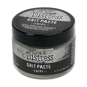Könnte beinhalten: Ein Tiegel Distress Grit Paste in der Farbe Crypt. Der Tiegel hat einen schwarzen Deckel und ein silbernes Etikett mit Produktname und Beschreibung. Die Paste ist eine getönte, transluzente Farbe mit schwarzen Flecken. Der Tiegel enthält 88,7 ml.