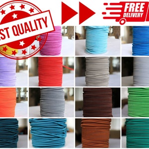 May include: A variety of colours of elastic cord spools, including yellow, pink, purple, red, orange, grey, brown, green, teal, blue, and orange. The spools are arranged in a grid pattern on a white surface.