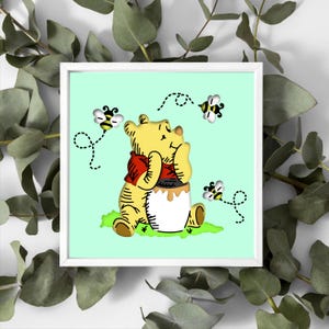 May include: A framed print depicting a yellow bear in a red shirt, seated beside a honey pot. Three cartoon bees with black and yellow stripes fly around the bear. The background is a pale green colour.