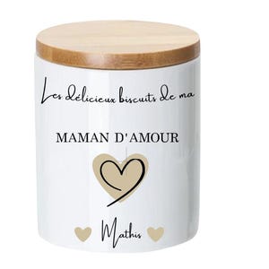 Peut inclure: Une boîte à biscuits en céramique blanche avec un couvercle en bambou. La boîte est ornée d'une inscription noire qui dit "Les delicieux biscuits de ma MAMAN D'AMOUR" avec un cœur et le nom "Mathis" en dessous.