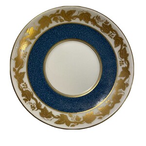 Puede incluir: Un platillo blanco con un borde azul y dorado. El borde está decorado con un patrón de vid dorado.