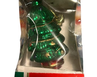 May include: A green glass Christmas tree ornament in a clear plastic box. The ornament is hand-blown and has gold accents. The box has red and green accents with the text "Classic Glass Ornament" and "Hand Blown".