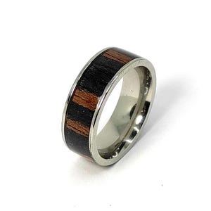 May include: A silver ring with a black and brown wood inlay. The ring is a simple design with a smooth finish.