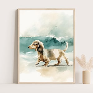 May include: Watercolour print of a dachshund dog on a beach. The dog is light brown and white, with a long body and short legs. The background features a teal ocean and a light blue sky. The artwork is framed in a light wood frame.
