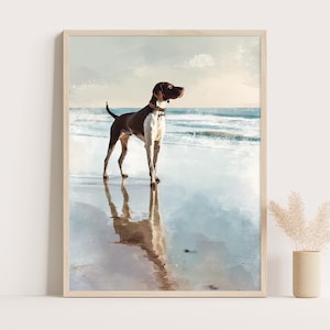 Puede incluir: Impresión enmarcada de un perro en una playa. El perro, marrón y blanco con collar rojo, está de pie sobre arena mojada. El mar y el cielo forman el fondo, con el reflejo del perro visible.