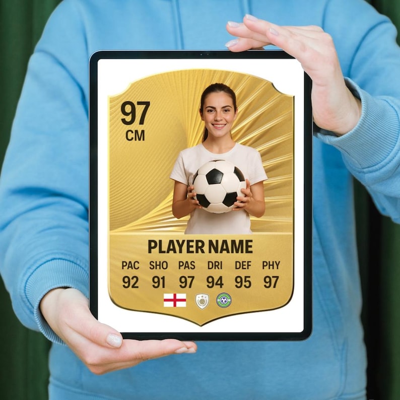 May include: A tablet showing a soccer player card with a gold design. The card displays a woman holding a soccer ball, with the number "97" and the letters "CM" at the top. Below, it reads "PLAYER NAME" and lists player stats.