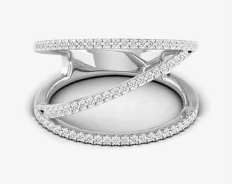 May include: A silver ring with a unique design. The ring features a band that wraps around the finger, with a second band crossing over it. Both bands are encrusted with small, sparkling stones, creating a dazzling effect. The ring is set against a white background.