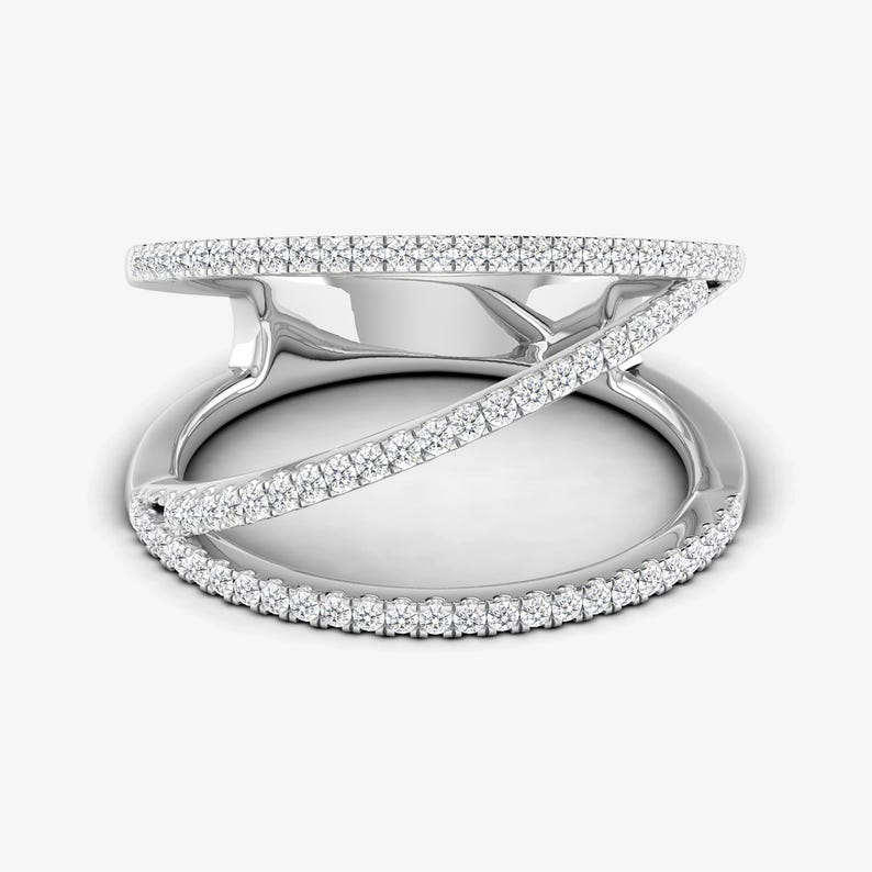 Puede incluir: Un anillo de plata con un dise&ntilde;o &uacute;nico. El anillo presenta una banda que rodea el dedo, con una segunda banda que la cruza. Ambas bandas est&aacute;n incrustadas con peque&ntilde;as piedras brillantes, creando un efecto deslumbrante. El anillo est&aacute; sobre un fondo blanco.