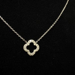 May include: A silver chain necklace with a four-leaf clover pendant encrusted with small clear stones.