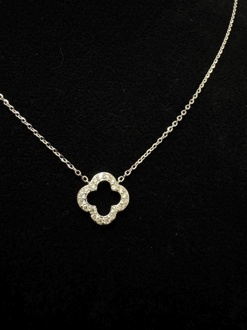 May include: A silver chain necklace with a four-leaf clover pendant encrusted with small clear stones.