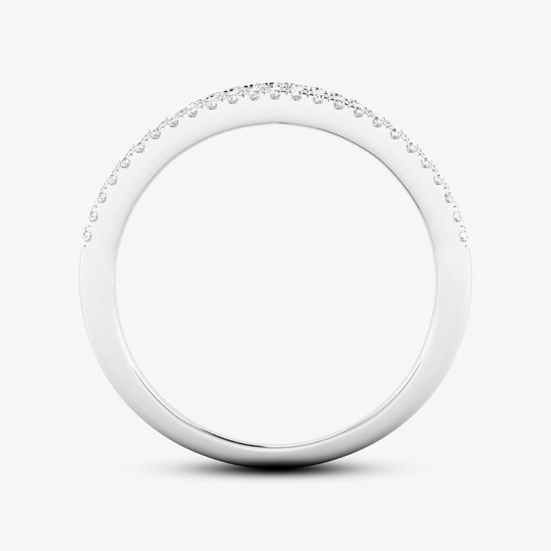 Puede incluir: Un anillo de metal blanco con una banda curva, engastado con peque&ntilde;as piedras preciosas claras en la parte superior. El anillo se muestra sobre un fondo liso y claro, resaltando su superficie pulida y el brillo de las piedras. Una joya.