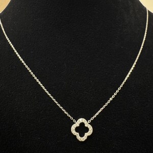 May include: A silver chain necklace with a four-leaf clover pendant encrusted with small clear stones.