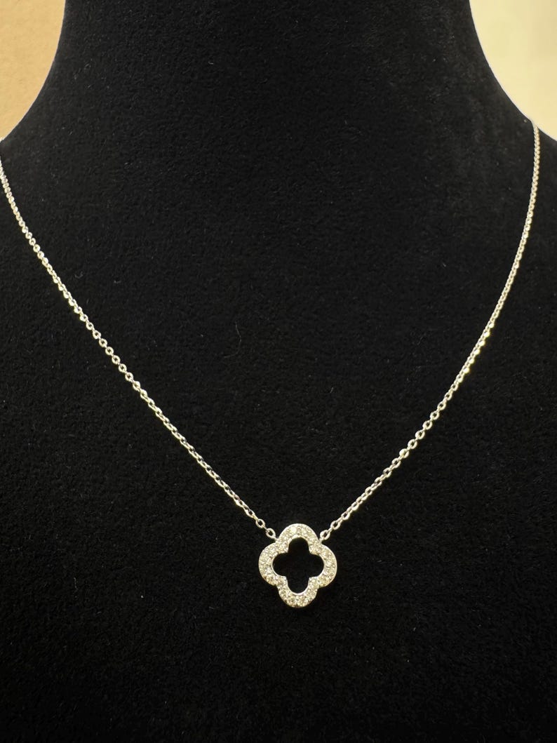 May include: A silver chain necklace with a four-leaf clover pendant encrusted with small clear stones.