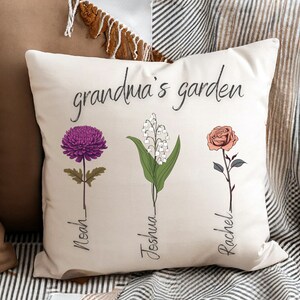 May include: White throw pillow with the text "grandma's garden" and three floral illustrations. The flowers are a purple chrysanthemum, a cluster of white lily of the valley, and a pink rose. Each flower has a name written below it: Noah, Joshua, and Rachel.