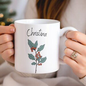 May include: White ceramic mug with a green holly sprig and red berries design. The mug has the name "Christina" written in black cursive on the front.